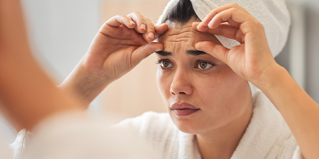 Frau am Spiegel berührt Falten auf der Stirn