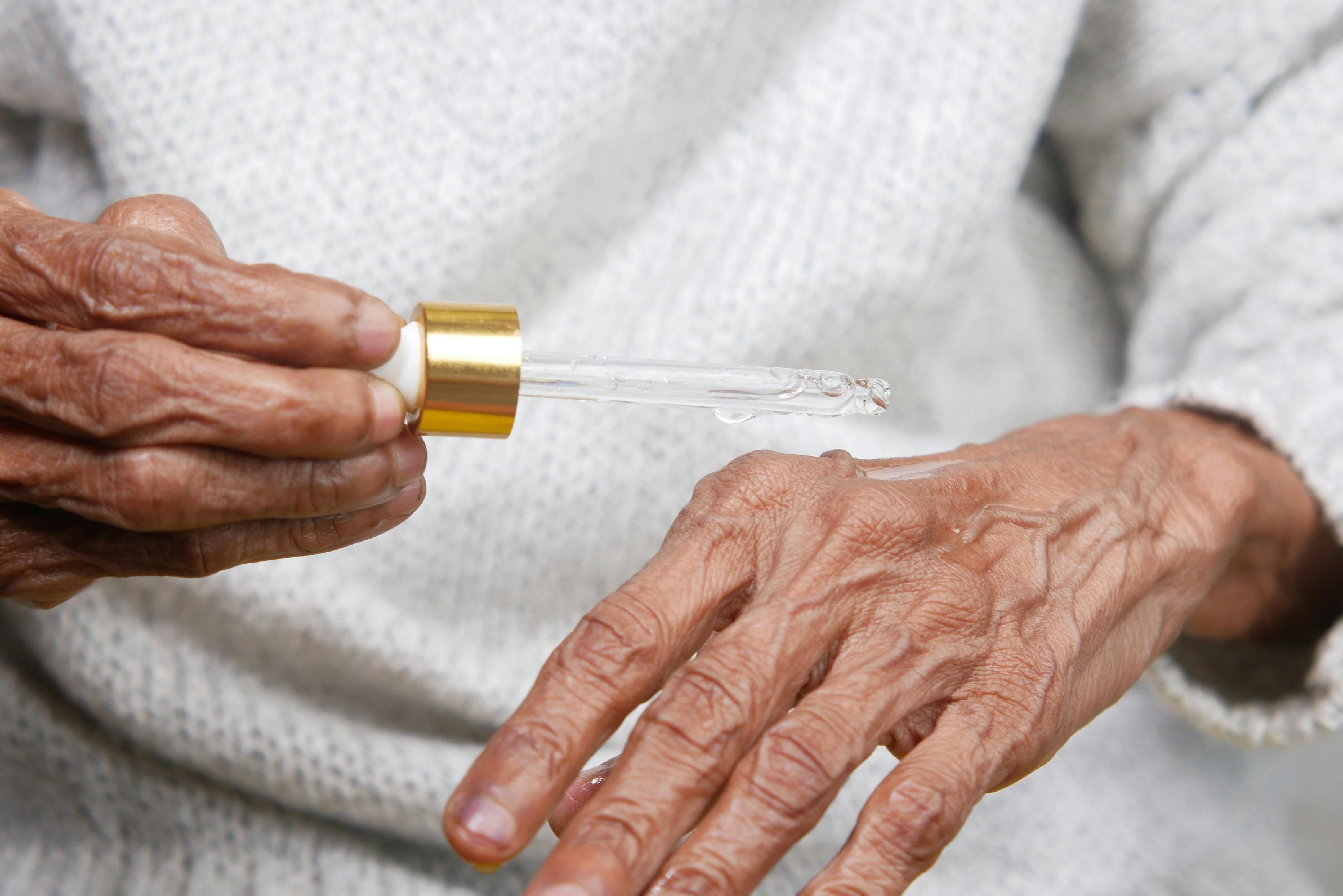 Eine ältere Person tropft mit einer Pipette ein Pflege-Serum auf ihren Handrücken.