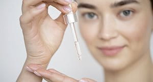 Frau mit Pipette tropft Serum auf Handfläche