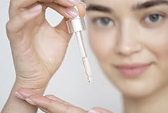 Frau mit Pipette tropft Serum auf Handfläche