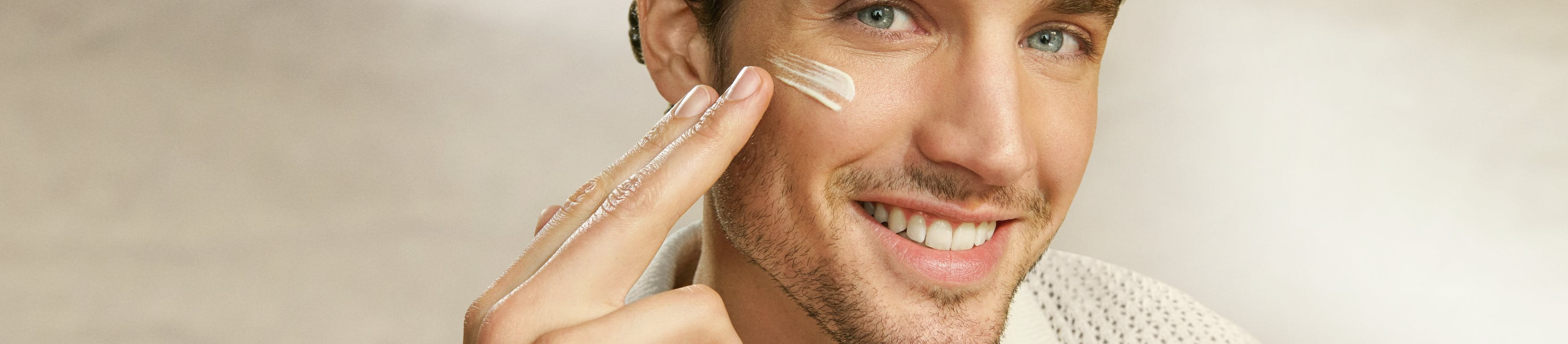 Man smiling and applying sunscreen to his cheekbone while he looks into the camera