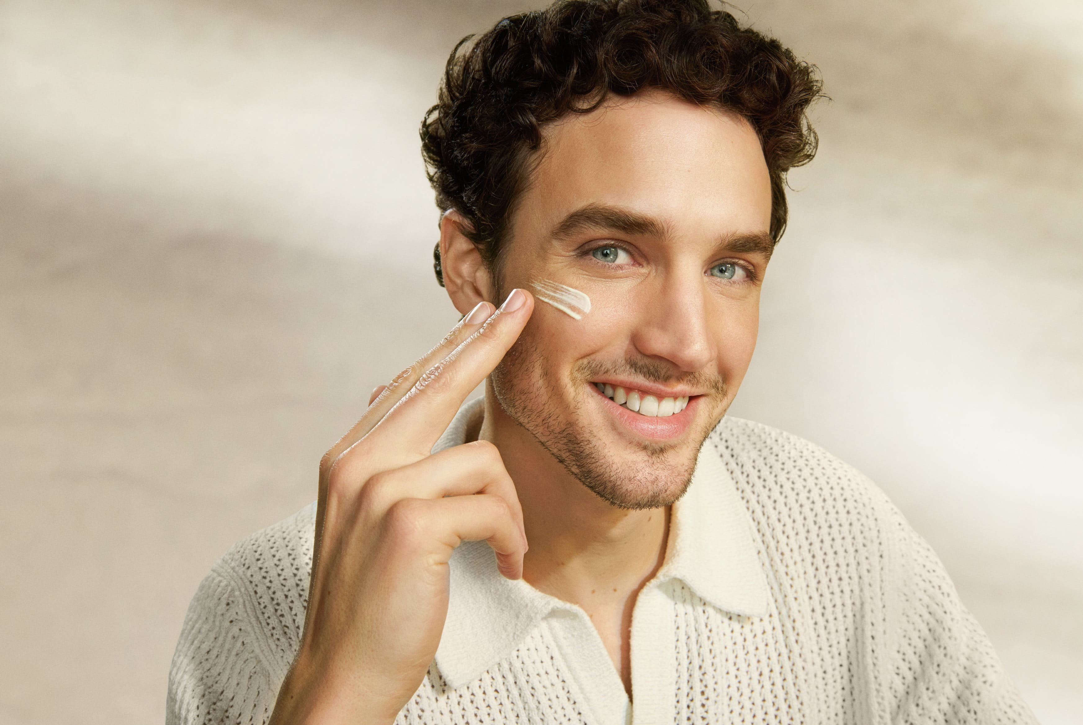 Man smiling and applying sunscreen to his cheekbone while he looks into the camera