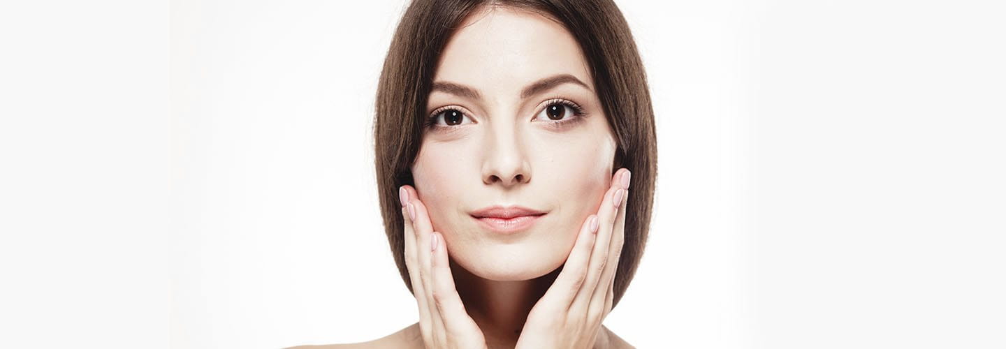 Ritratto di donna con pelle curata, tocco leggero della mano sul viso come segno di cura.