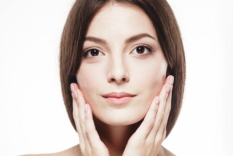 Ritratto di donna con pelle curata, tocco leggero della mano sul viso come segno di cura.