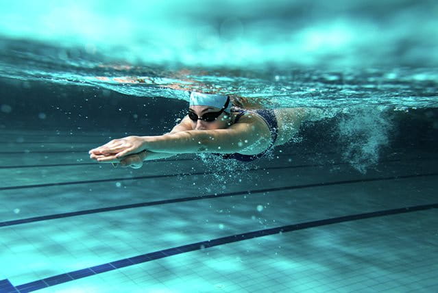 Nuotatrice sott'acqua in piscina mentre esegue una bracciata, indossando occhialini e cuffia