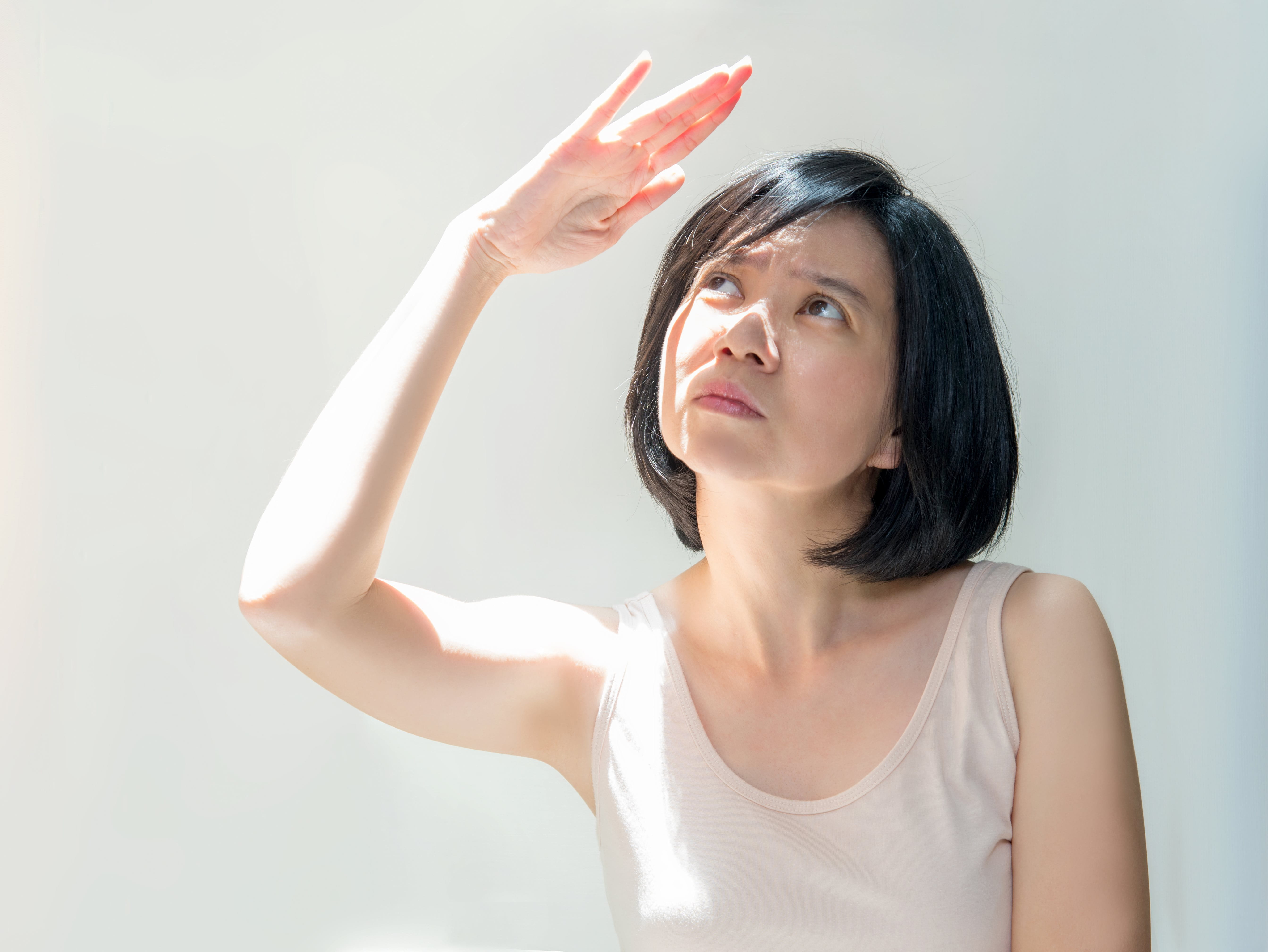 Eine junge Frau mit heller Haut hält sich die Hand über den Kopf, um Sonnenstrahlen abzuschirmen.