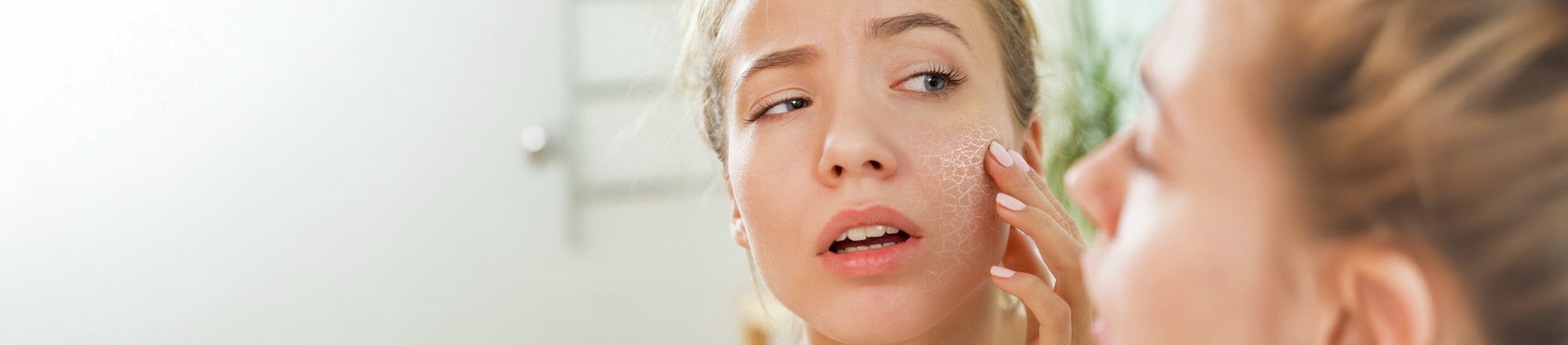 Ragazza osserva la pelle secca e screpolata allo specchio