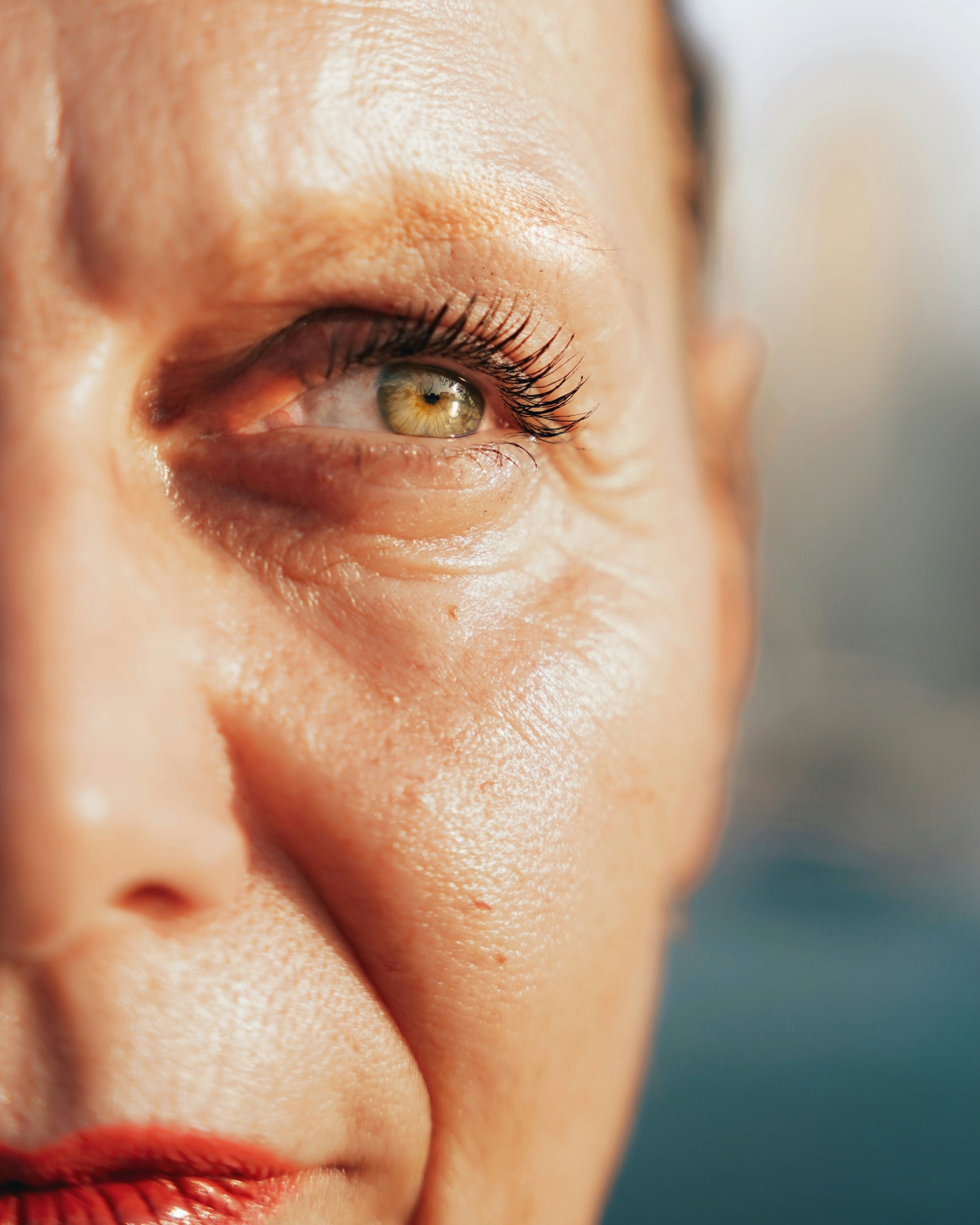 Gros plan sur la moitié droite du visage d'une femme à la peau claire, exposée au soleil. Sa peau, qui s'affine, présente des rides et ridules.