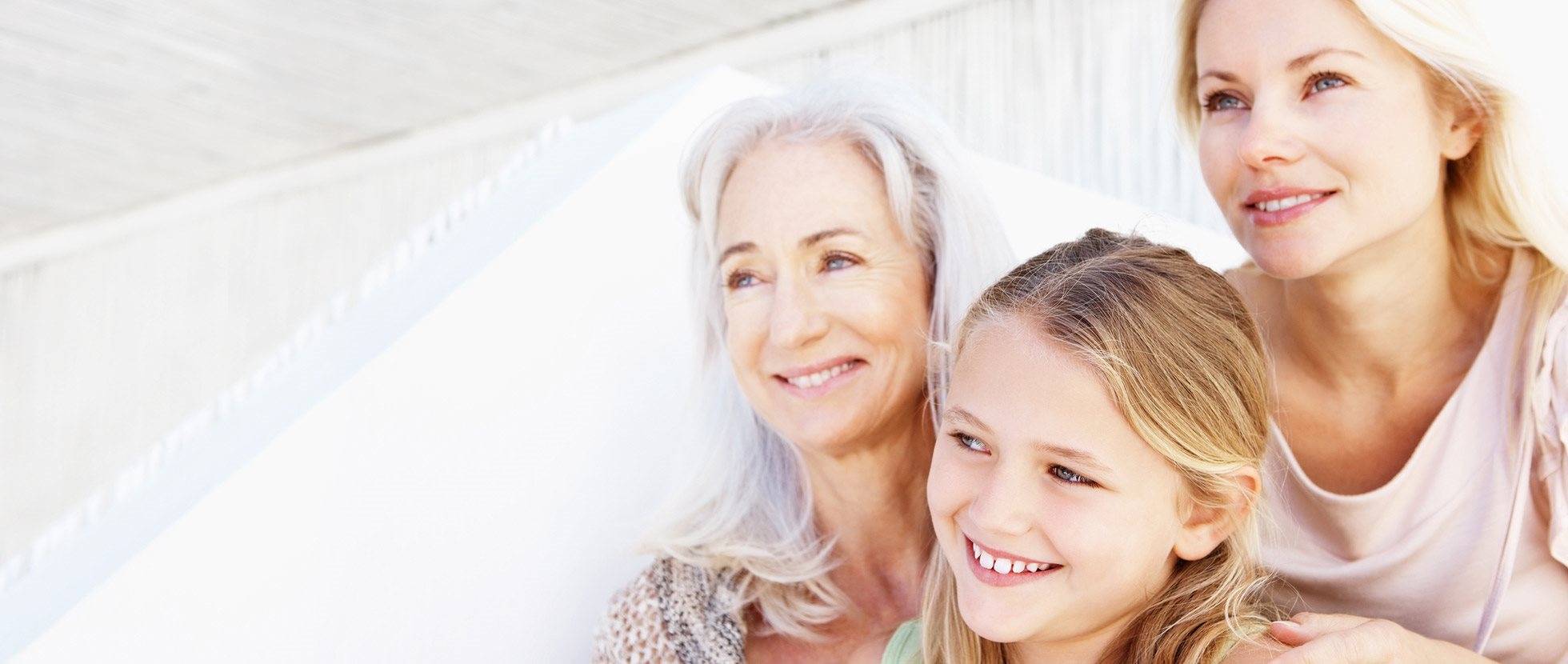 Three generations of women with healthy skin smiling outdoors.