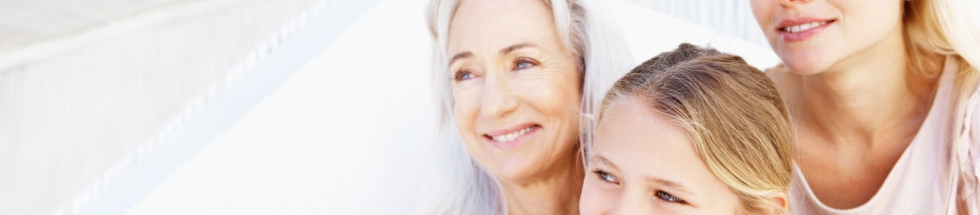 Three generations of women with healthy skin smiling outdoors.