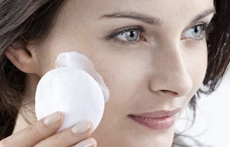 Woman cleansing face with cotton pad.