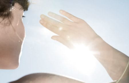 Woman holding one hand in front of her face to protect from sun