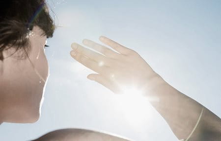Frau schirmt mit der Hand ihr Gesicht vor der Sonne ab  Titel: Gesicht vor Sonne und Sonnenbrand schützen