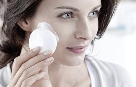 Woman applying cleanser on face with cotton pad.