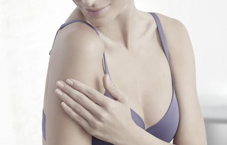 Woman wearing a bra is touching her right arm.