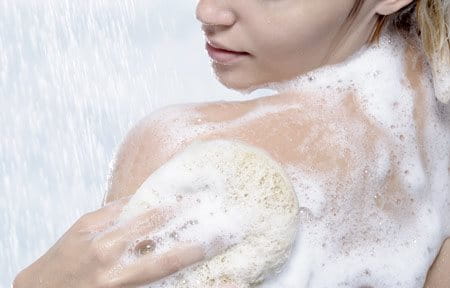 Frau seift sich beim Duschen den Rücken ein und beugt so Pickeln am Rücken vor. 