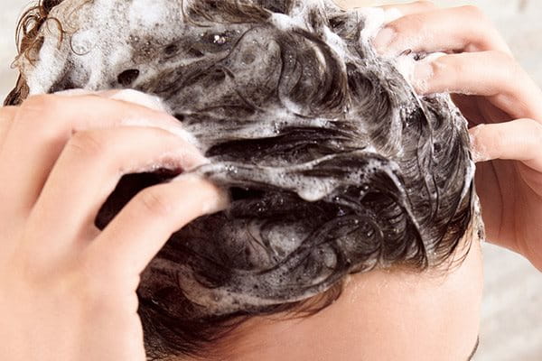 Vrouw die shampoo gebruikt voordat ze de behandelende verzorging voor dunner wordend haar opbrengt