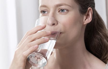 Frau, die ein großes Wasserglas an die Lippen führt