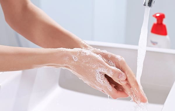 Eingeseifte Hände, die unter einen laufenden Wasserhahn gehalten und abgewaschen werden. 