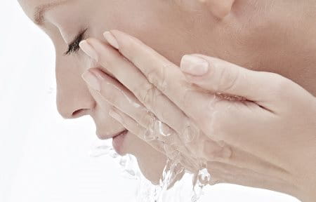 Woman washing face with water.