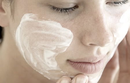 Woman applying cream on her face.	