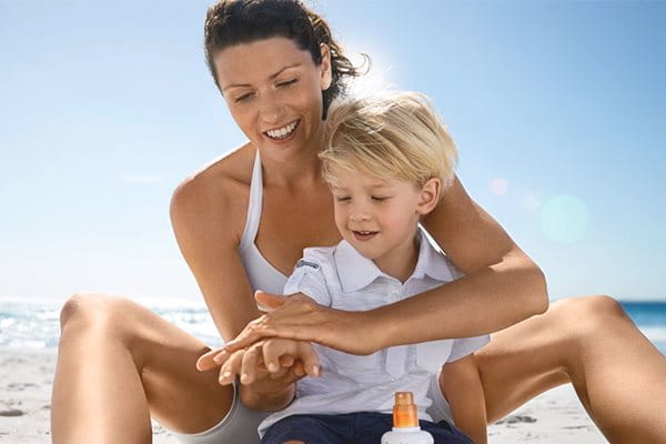 Kvinna som smörjer in sitt barn med Eucerin Sun Kids på en strand