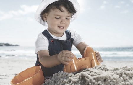 Kleinkind mit Hut spielt in der Sonne am Strand