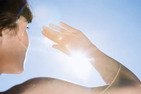 Kvinna som skyddar sig med handen från solens strålar för att illustrera solskydd