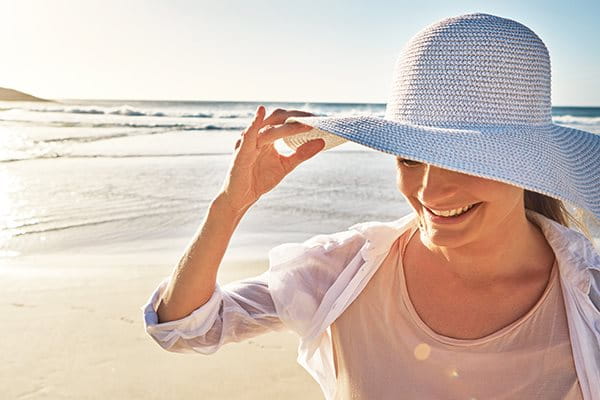 Kvinna i solhatt på en strand i skyddande kläder