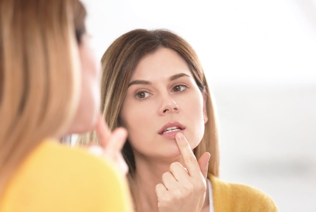 Junge Frau greift mit Zeigefinder an ihre Unterlippe