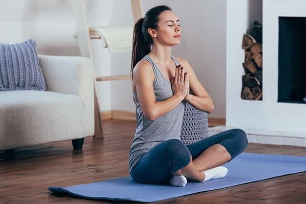 Eine Frau beim Meditieren im Schneidersitz auf einer Yogamatte