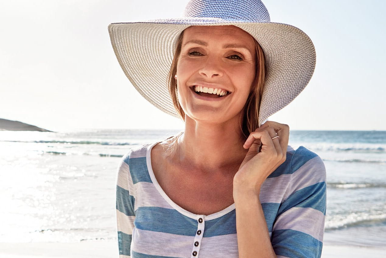 Frau am Strand mit Hut lächelt