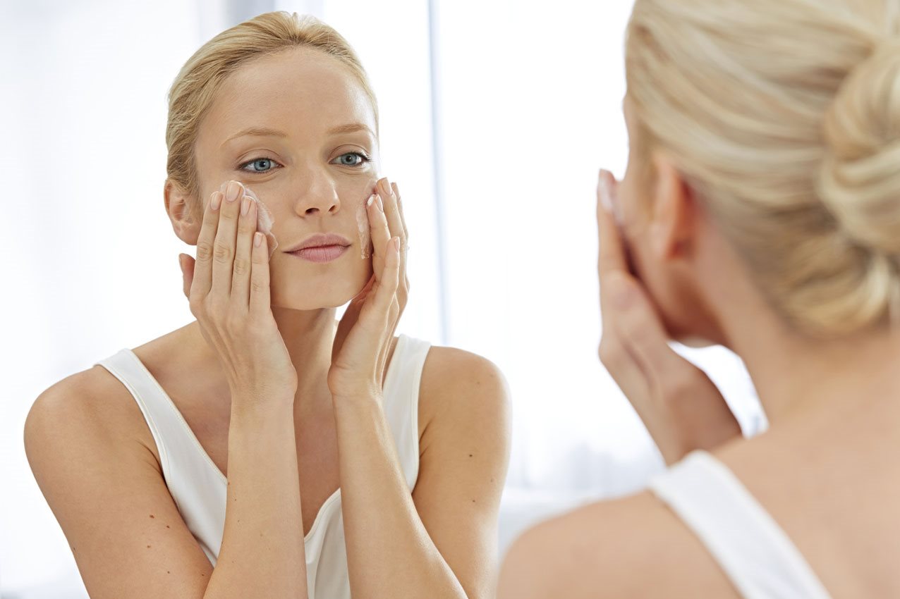 Junge blonde Frau cremt sich das Gesicht ein