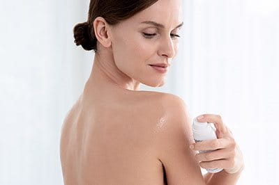 Eine Frau sprayt sich mit dem Atopi Control Anti-Juckreiz Spray von Eucerin die rechte Schulter ein, um die Symptome von Hautausschlag zu mindern. 