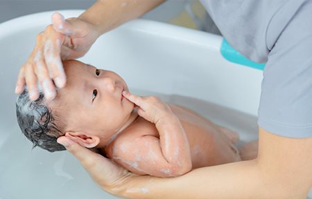 Eine Mutter wäscht den Kopf ihres Babys mit einem Shampoo. 
