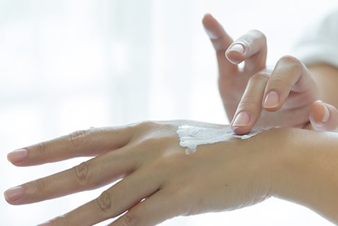 Jemand mit Neurodermitis an der Hand cremt die Hände ein