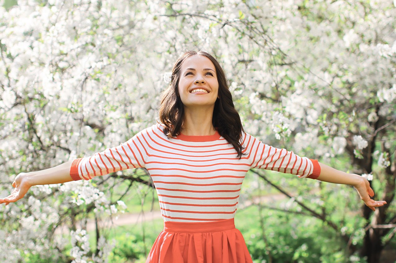 Junge Frau steht unterm Kirschenbaum und lächelt