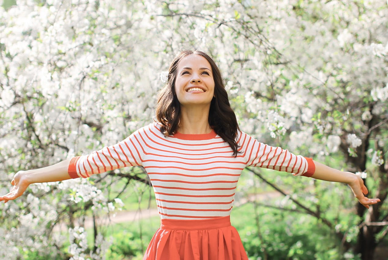Junge Frau steht unterm Kirschenbaum und lächelt