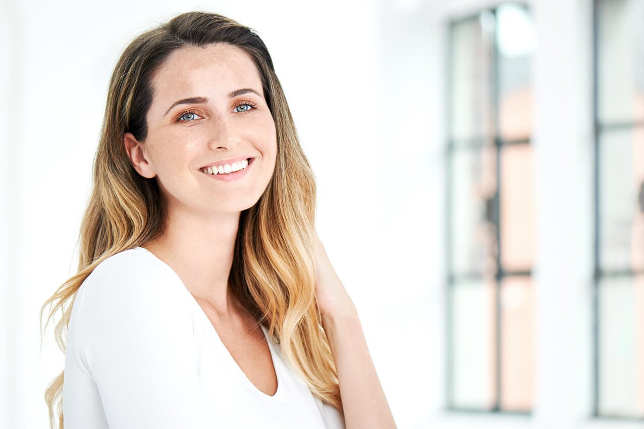 Junge Frau mit hellem welligen Haar und weißem Shirt lächelt 