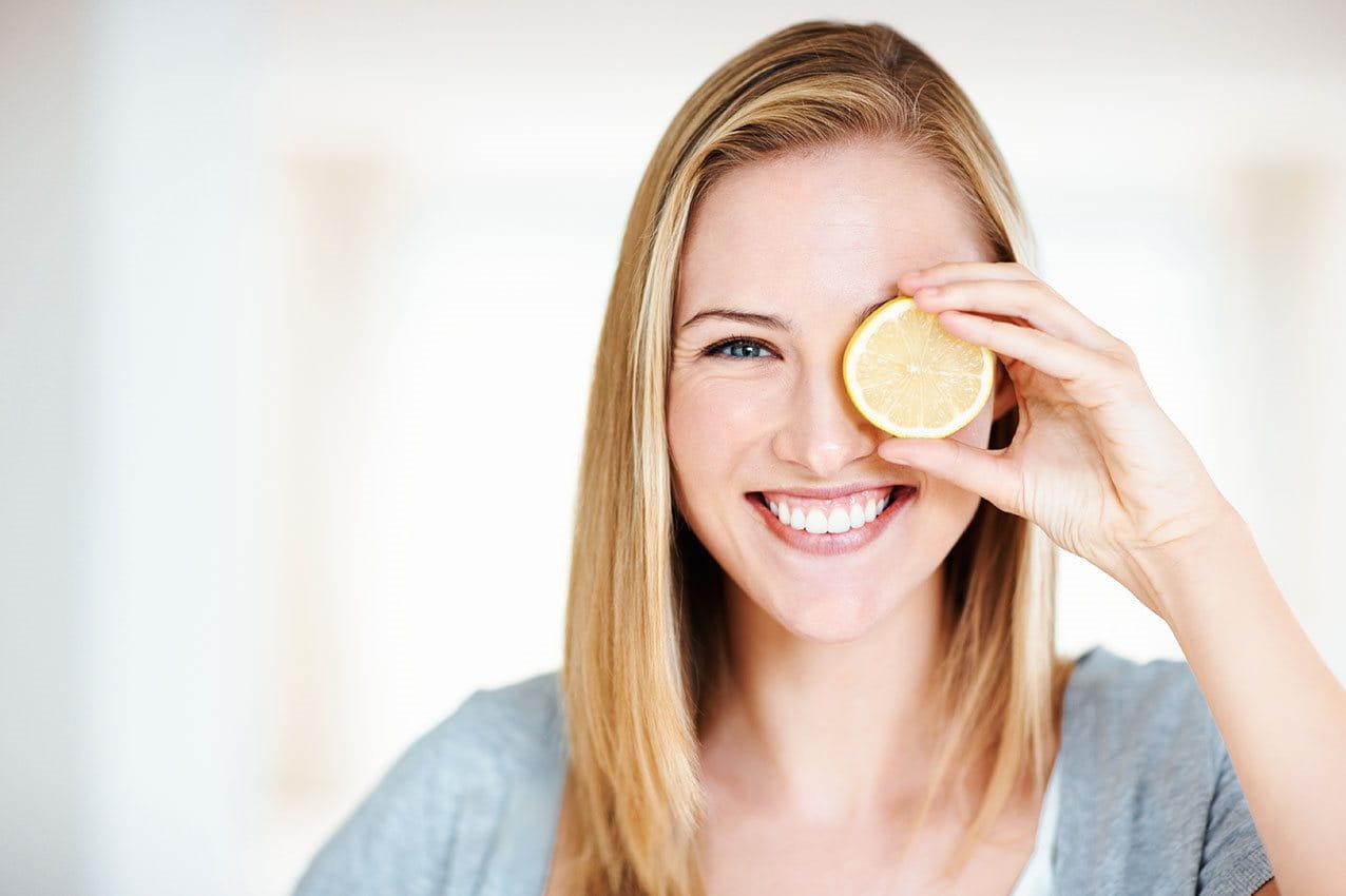 Frau hält Zitrone vor das linke Auge