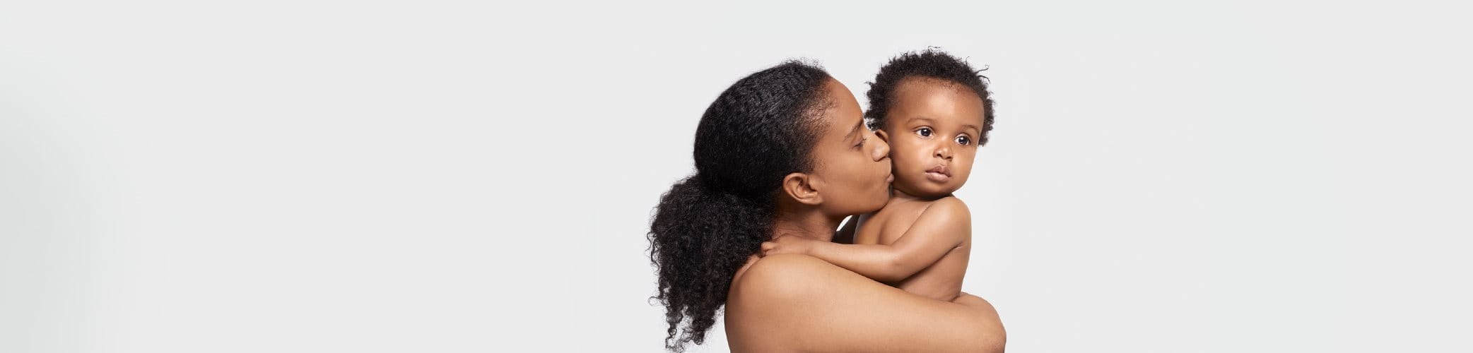 Mannequin féminin portant un petit enfant dans ses bras et l'embrassant sur la joue droite.