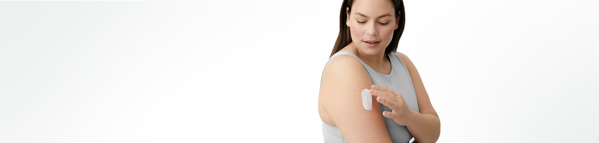A view of a female model with dark hair and wearing a grey coloured tank top looking downwards with a Eucerin cream product smeared on the model's right arm.