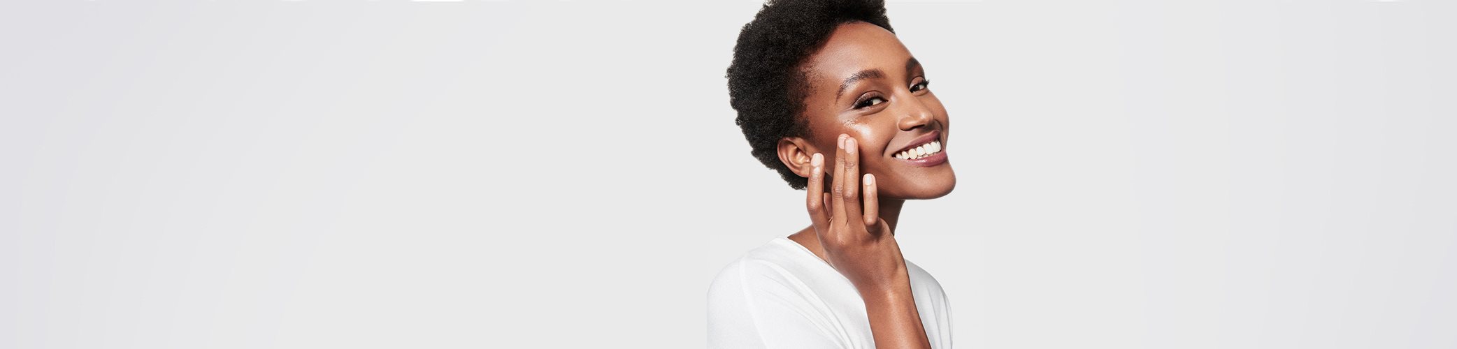 Vue rapprochée d'un mannequin féminin aux cheveux courts, fixant la caméra, visage souriant, les doigts pressant sur sa joue droite.
