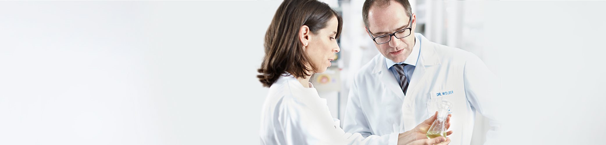 Mannequin masculin et mannequin féminin vêtus de blouses de laboratoire blanches, examinant un bécher rempli d'un liquide coloré que la femme tient dans ses mains.