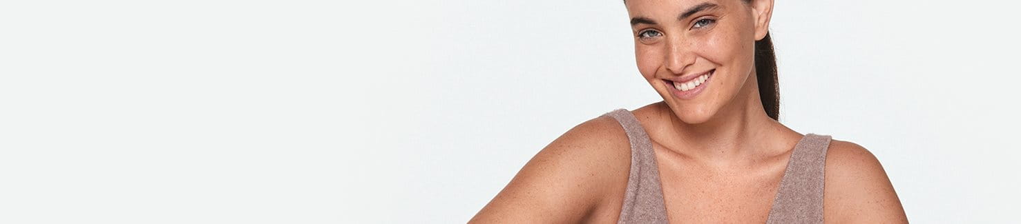 Mannequin aux cheveux longs rabattus vers l'arrière, visant souriant et vêtue d'un débardeur beige.