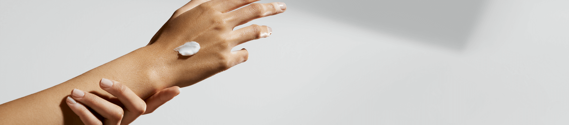 Un bras et une main s'étirent, tandis qu'on voit une touche de produit en crème sur la main.