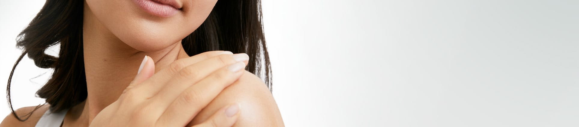 View of a female model with short dark hair touching her left shoulder and looking downwards against a white background.