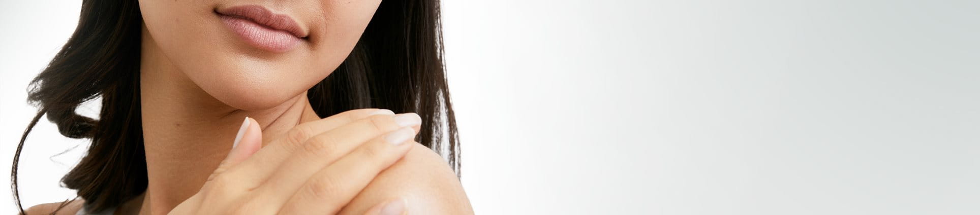 View of a female model with short dark hair touching her left shoulder and looking downwards against a white background.