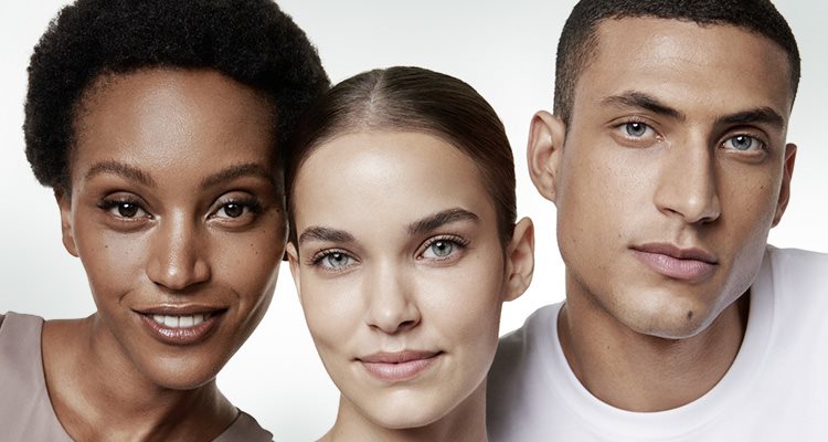 A closeup view of two female models and one male model wearing light coloured tops against a white background.
