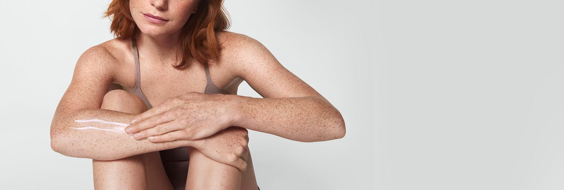 Une femme mannequin aux cheveux roux courts  étend une touche de produit en crème sur son bras droit.